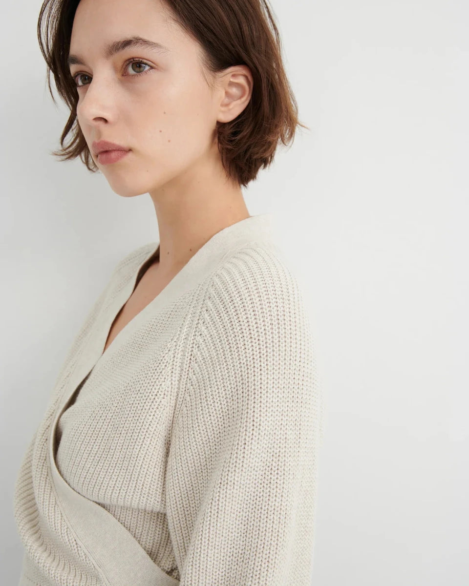 A woman with short brown hair wearing a cream-colored knit wrap cardigan, shown in a close-up profile against a light gray background.