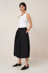 Woman wearing a white sleeveless top and black culottes on a beige background