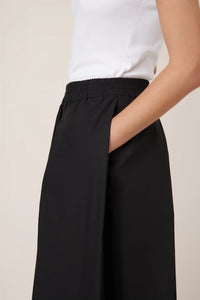 Black wide-leg culottes with side pocket  worn with a white top on a beige background