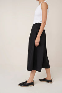 Person wearing a white top and black culottes on a plain background