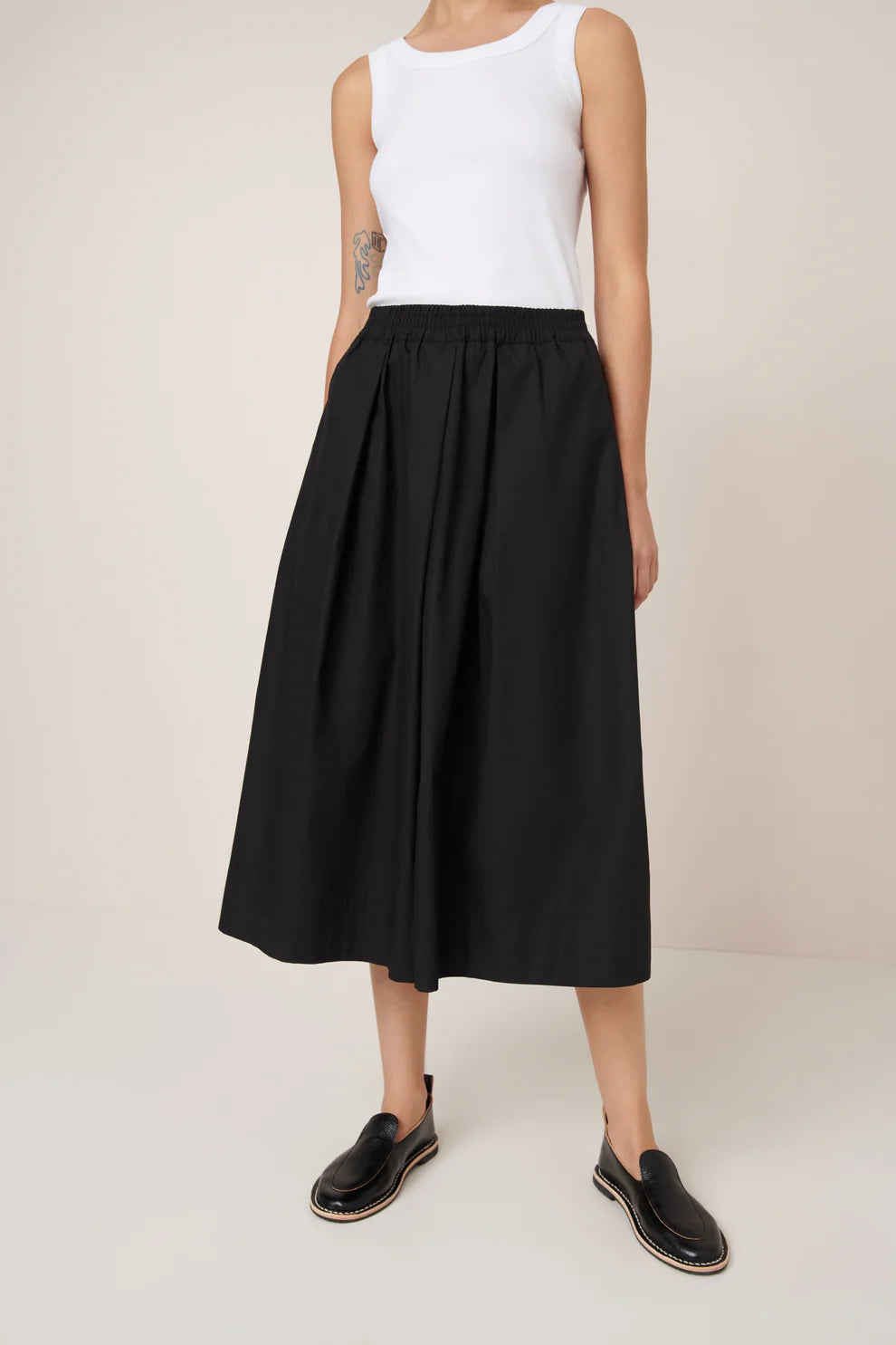 Person wearing black culottes and a white top on a plain background