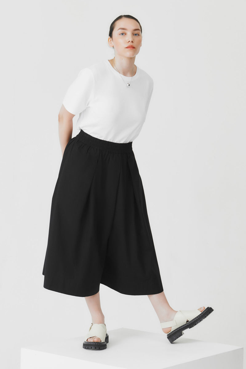 Person wearing a white top and black wide-leg culottes on a white background
