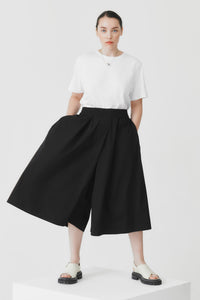 Person wearing a white top and black wide-leg culottes on a white background