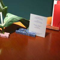 blue stone clip holding up a business card on a wooden surface with other objects