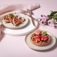Two plates of waffles with fruit on a pink surface