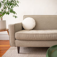 Beige sofa with a white round pillow in a living room setting