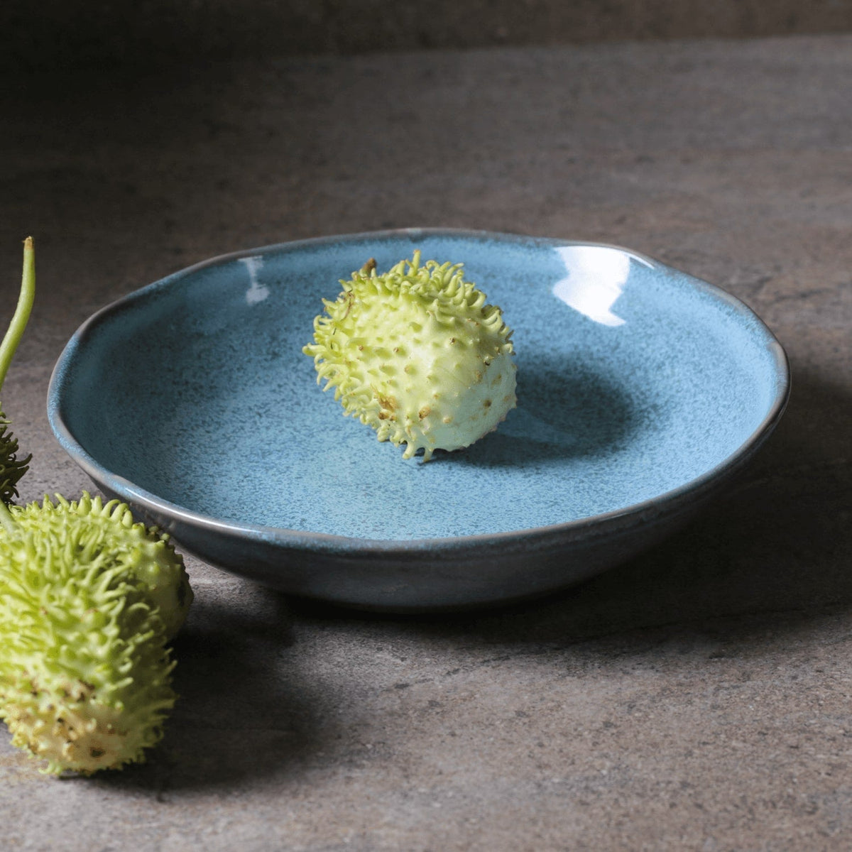 Blue ceramic plate with a green fruit-like object on a dark surface