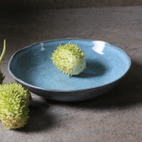 Blue ceramic plate with a green fruit-like object on a dark surface