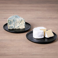 Two black plates with different types of cheese on a wooden surface