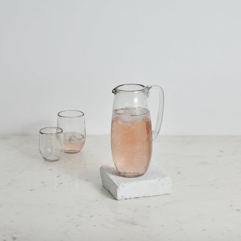 Pebbled Glass pitcher and two glass cups on a white surface