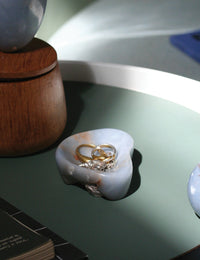 Light blue stone dish holding jewelry on a sage green surface with other objects and light