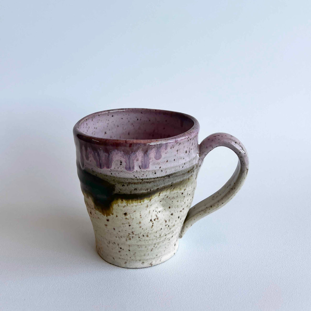 Ceramic mug with light and dark neutral and pink glaze details on a white background