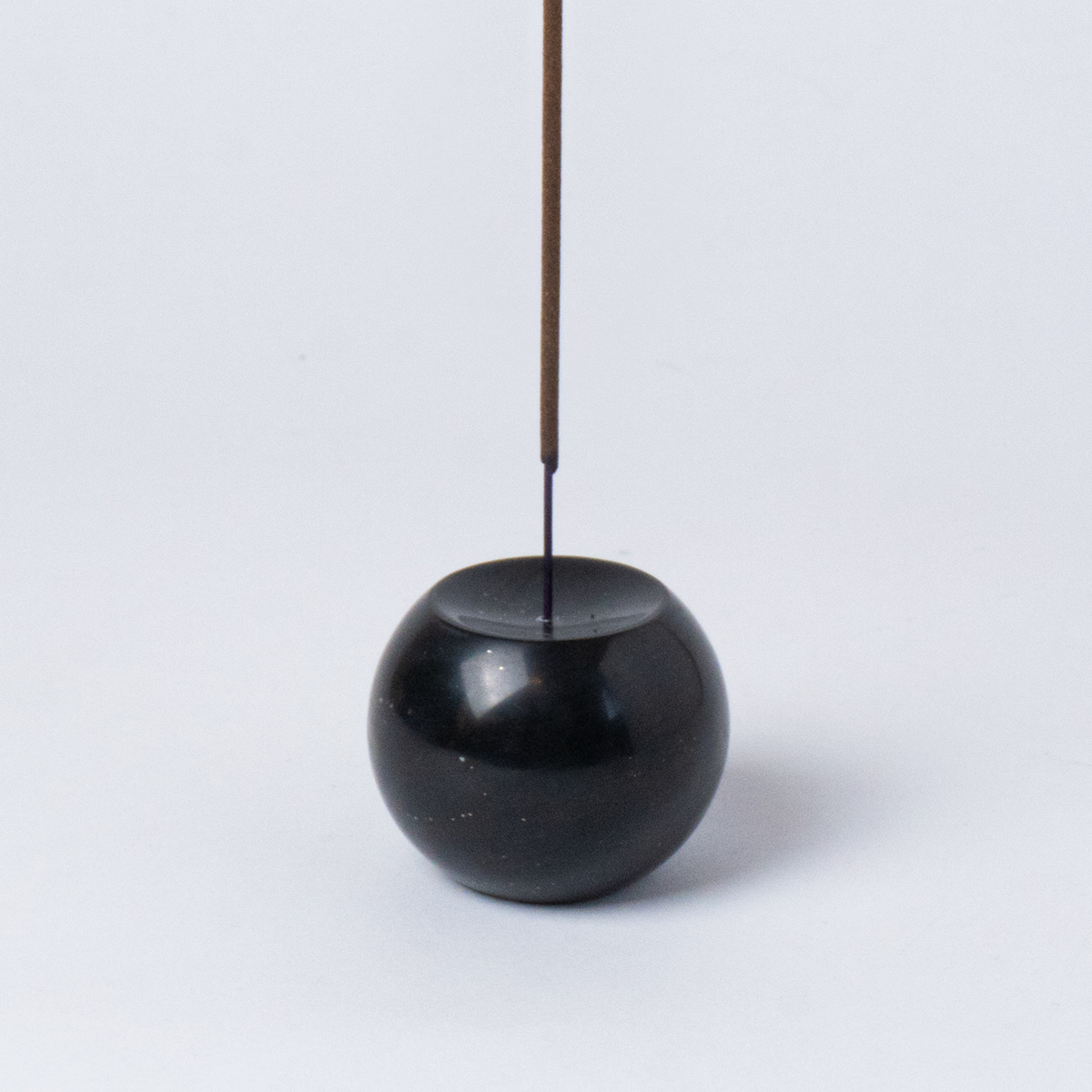 Black spherical incense holder with a single incense stick on a white background
