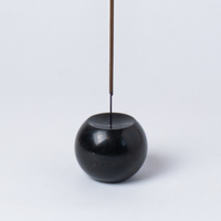 Black spherical incense holder with a single incense stick on a white background