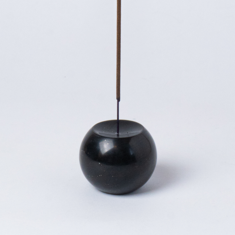 Black spherical incense holder with a single incense stick on a white background