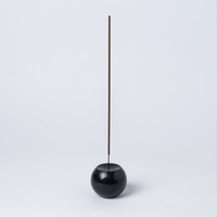 Black incense holder with a single incense stick on a light gray background