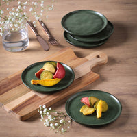 Green ceramic plates with food on a wooden table with a cutting board and small flowers.