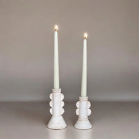 Two white candles in decorative candle holders on a neutral background