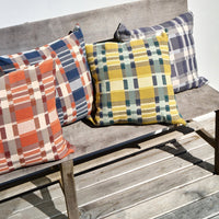 Four plaid patterned throw pillow cushions on a wooden bench outdoors.