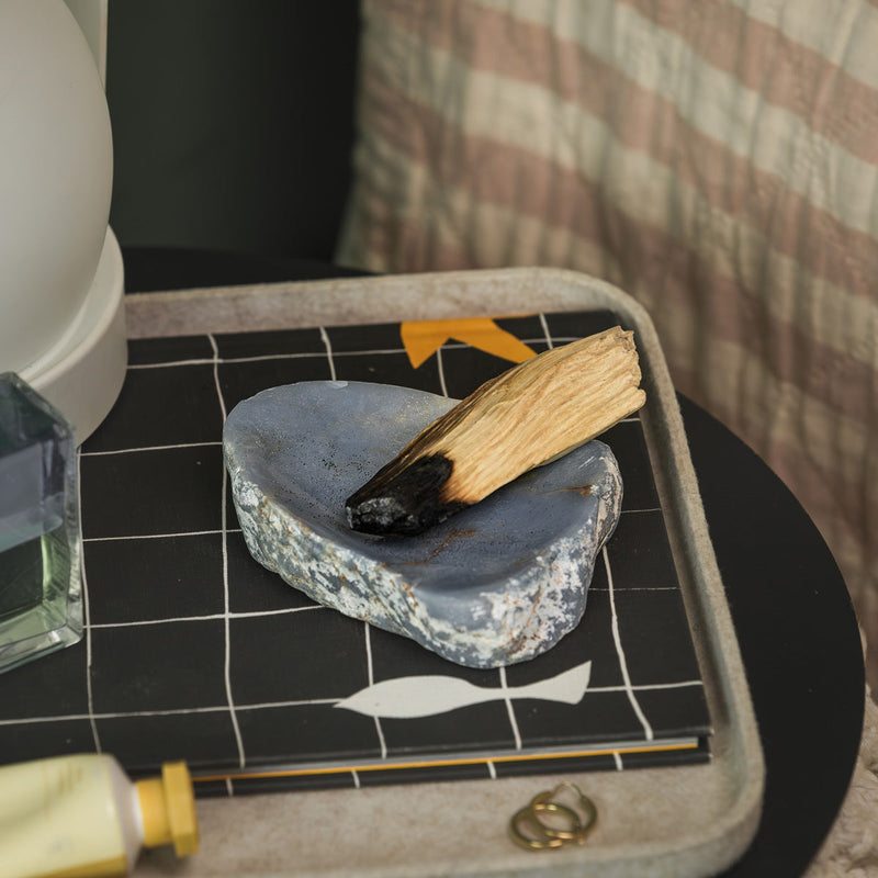 Small stone with a piece of palo santo on top, placed on a black tiled surface.