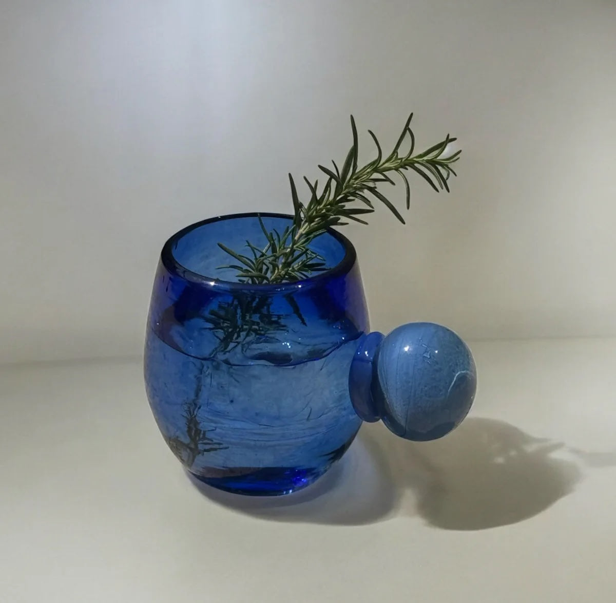 Blue glass cup with a rosemary sprig and drink on a white background