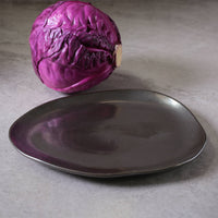 Purple cabbage next to a dark metallic plate against a neutral background