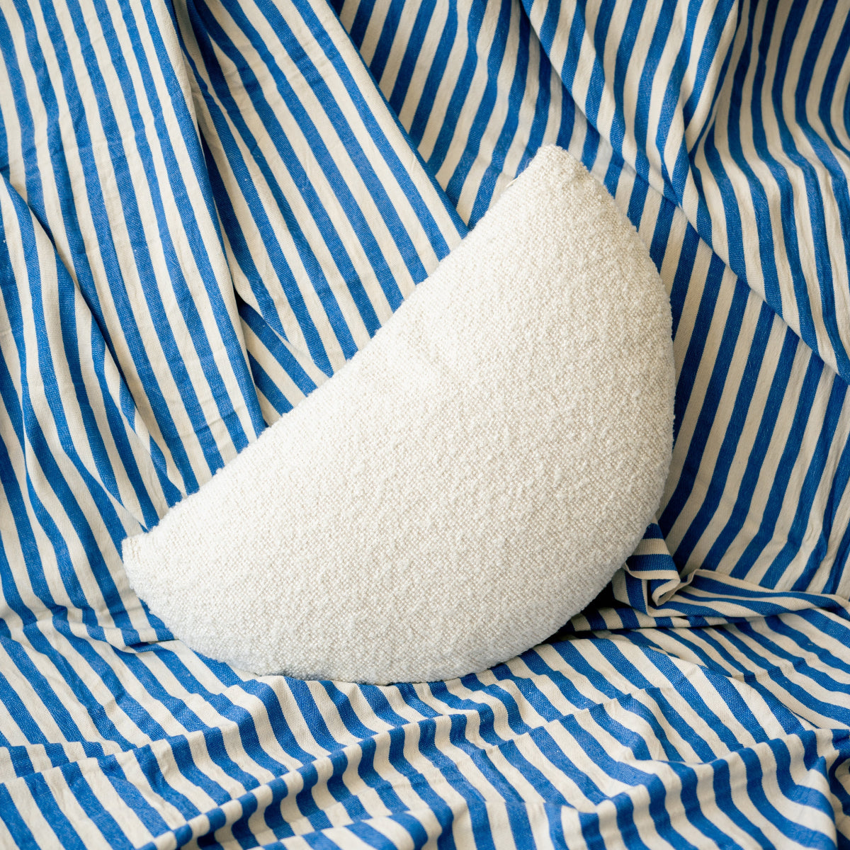 White crescent-shaped pillow on blue and white striped fabric