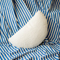 White crescent-shaped pillow on blue and white striped fabric