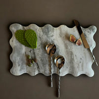 Marble cutting board with figs, leaves, and serving spoons on a brown background
