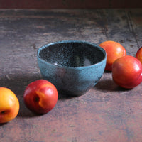 Blue ceramic bowl on a wooden surface with peaches around it