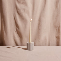 Taper candle in a textured holder against a beige fabric background
