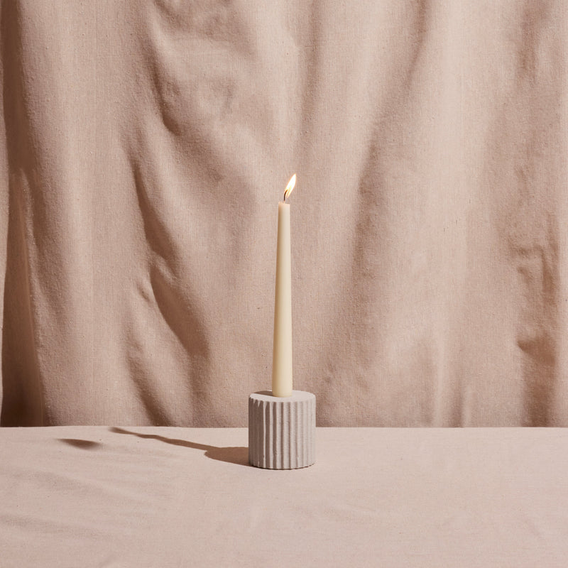 Taper candle in a textured holder against a beige fabric background