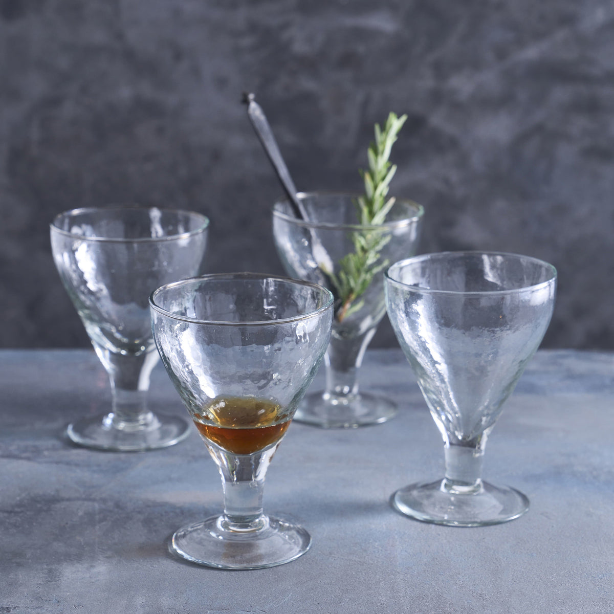 Set of clear glass goblets on a gray surface with a dark background