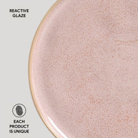 Close-up of a pink ceramic plate with reactive glaze texture on a light gray background.