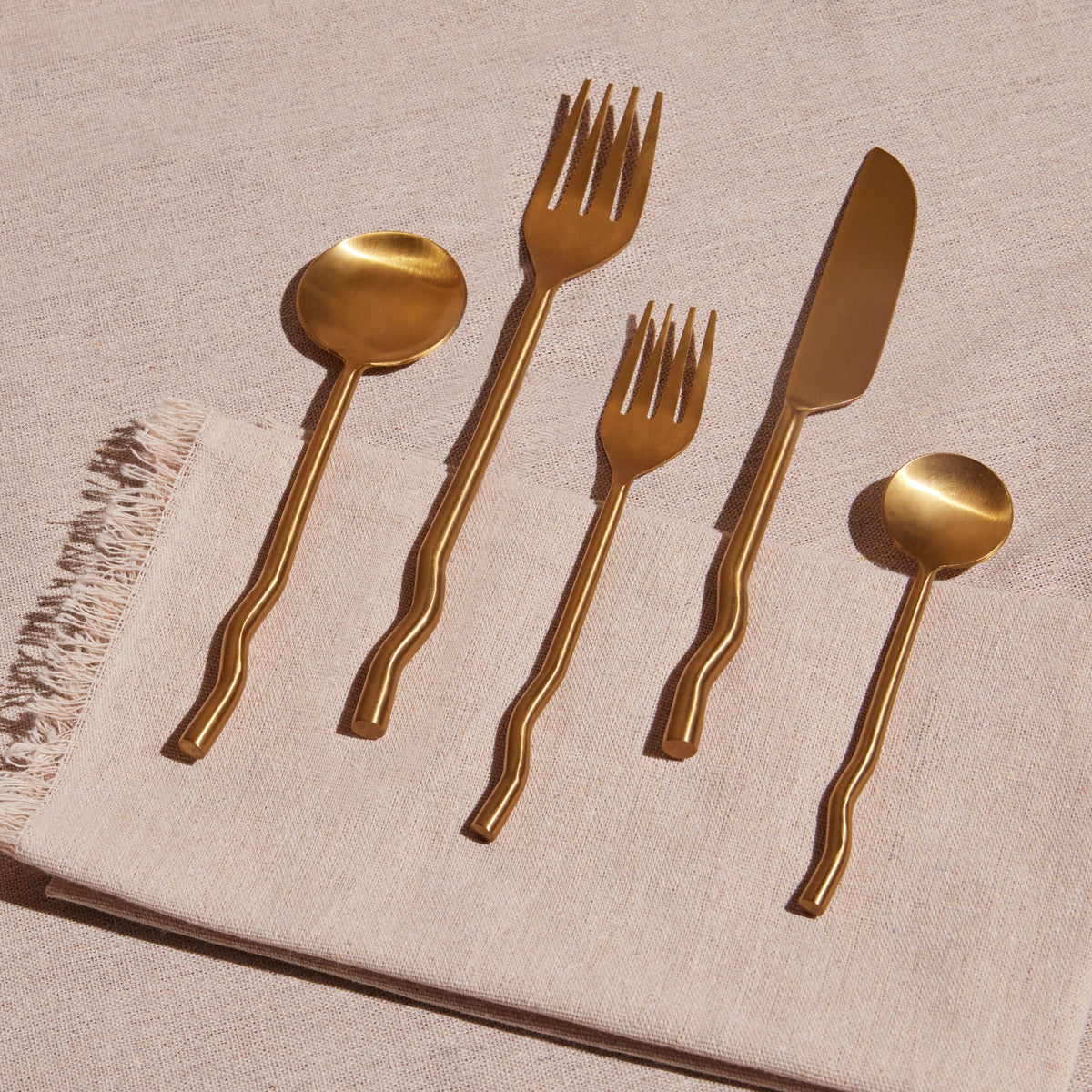 Set of brass cutlery including spoons, forks, and a knife on a textured surface.
