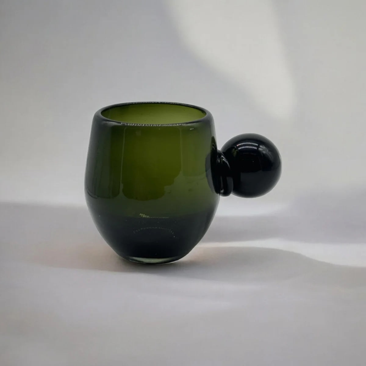 Green glass cup with a spherical handle on a white background