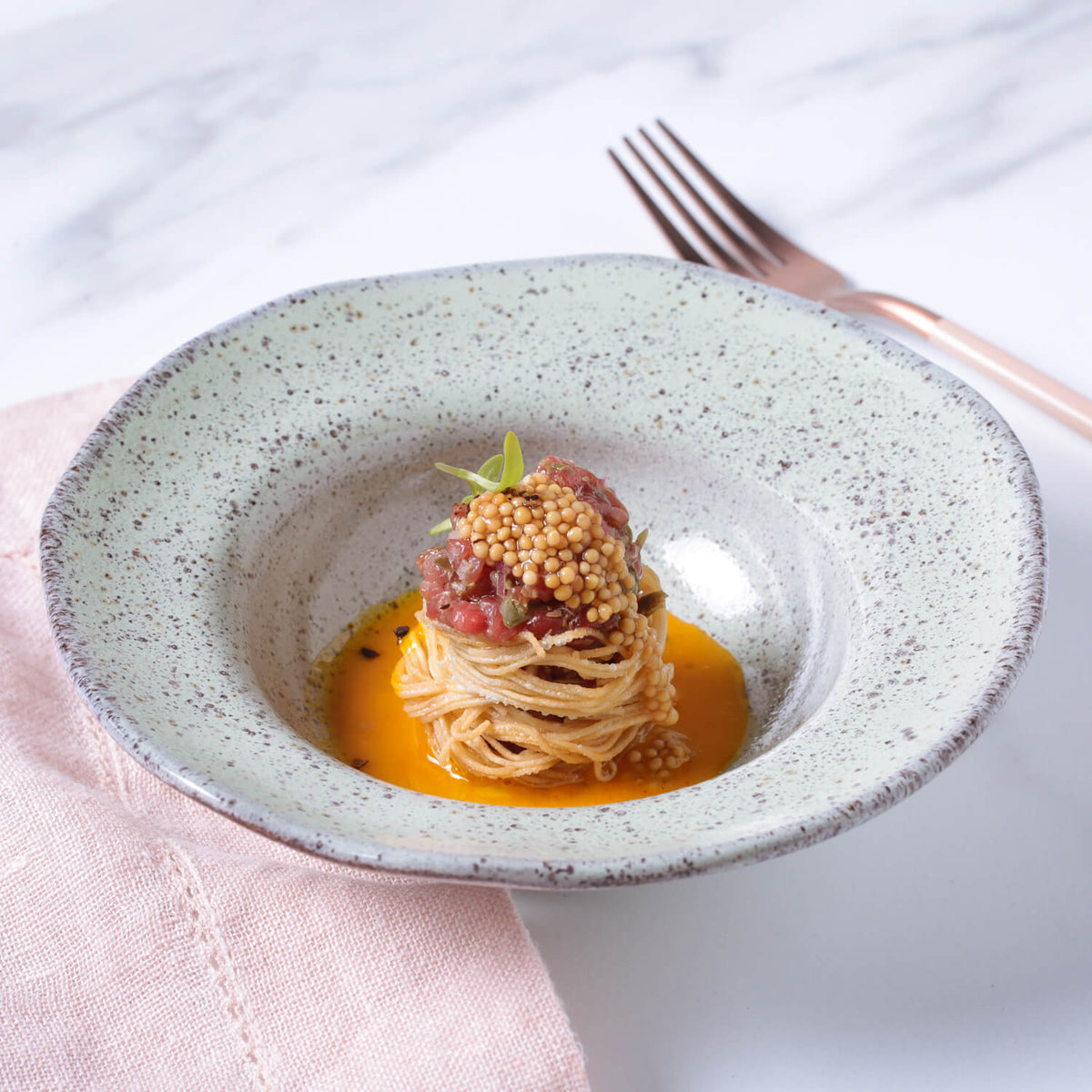 Delicate dish with garnishes on a textured ceramic plate, set against a light background.