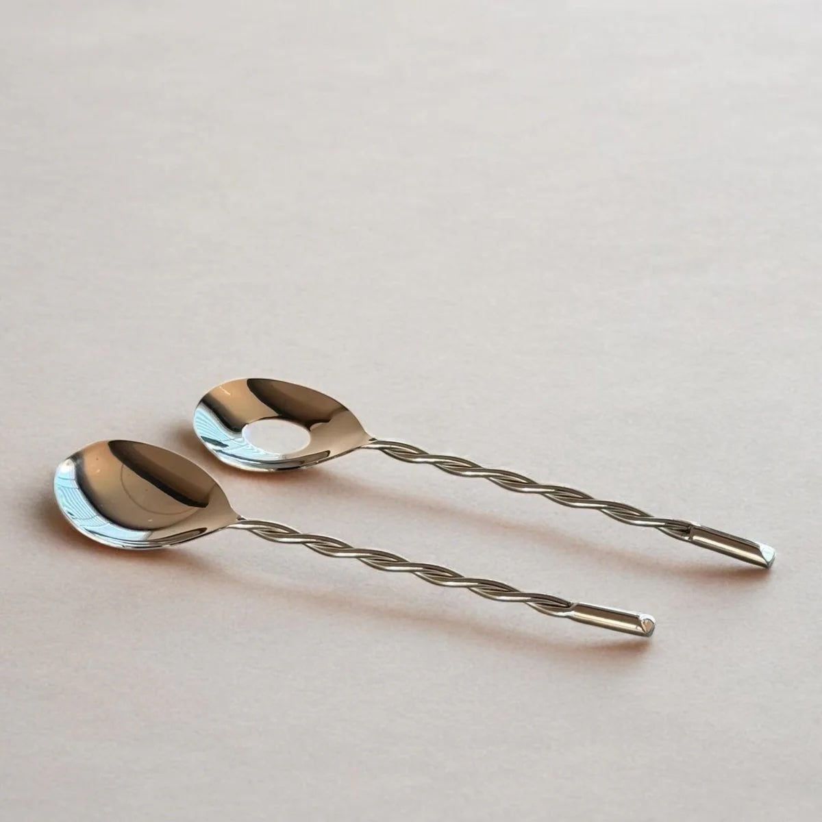 Two silver salad spoons with twisted handles on a light pink background