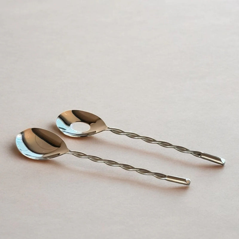 Two silver salad spoons with twisted handles on a light pink background