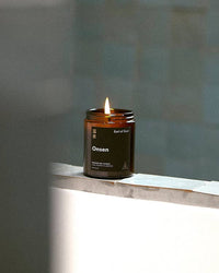 Lit glass jar candle with a label reading Onsen on the edge of a tiled surface