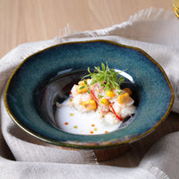 Delicate dish of seafood salad on a blue ceramic plate with garnishes, placed on a textured fabric surface.