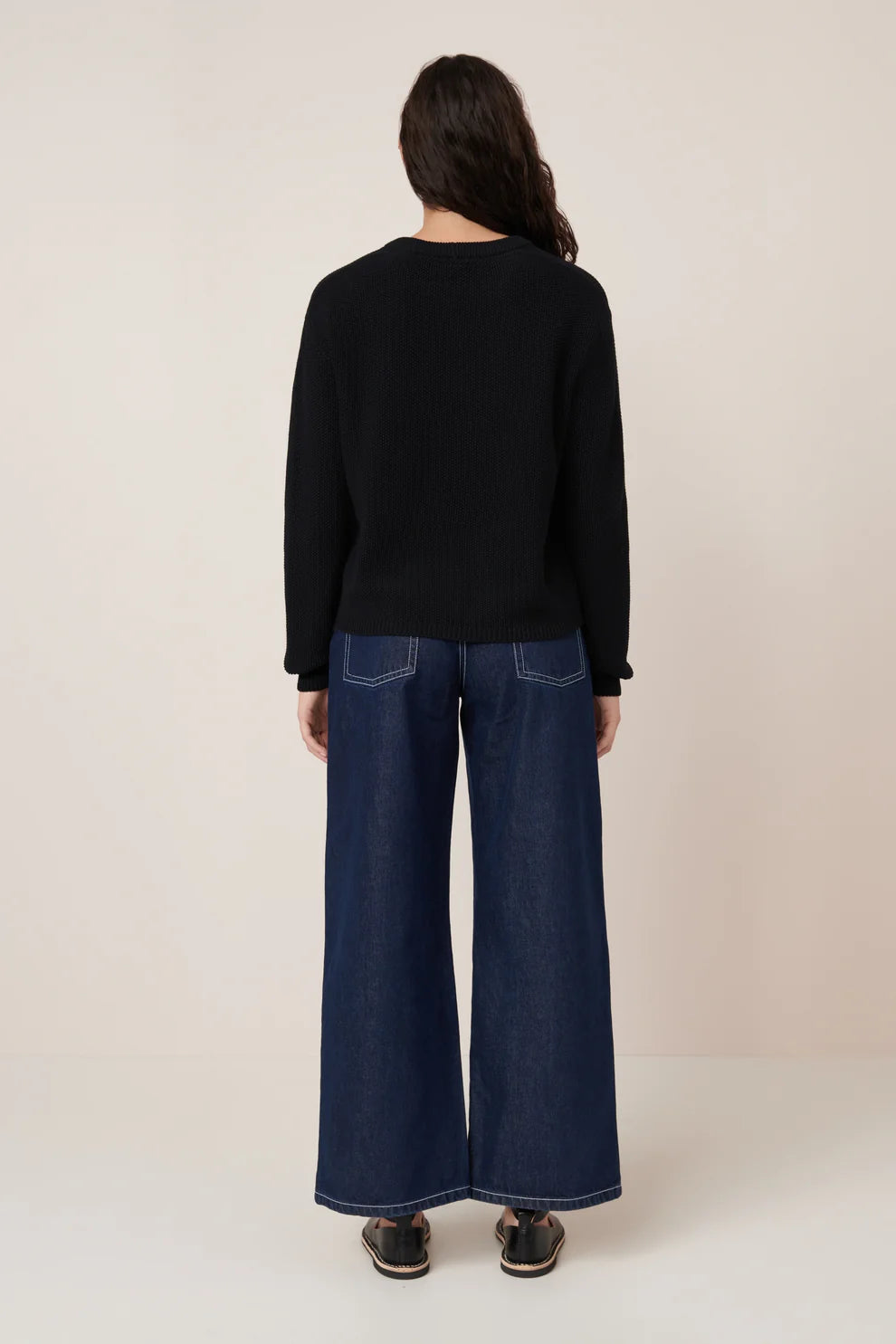 Person wearing a black sweater and blue jeans on a plain background