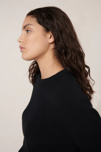 Woman wearing a black sweater against a plain background
