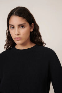 Woman wearing a black sweater against a plain background