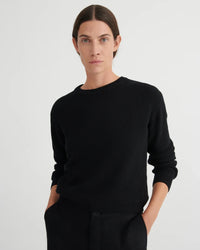 Person wearing a black sweater against a plain background