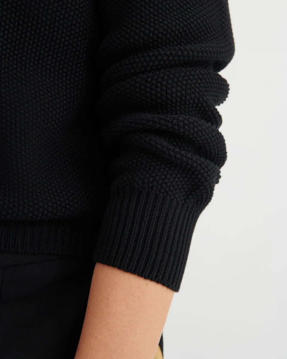 Close-up of a person wearing a black textured sweater on a light gray background