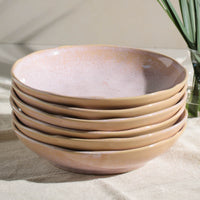 Stack of ceramic pasta plates with a beige and pink finish on a neutral background