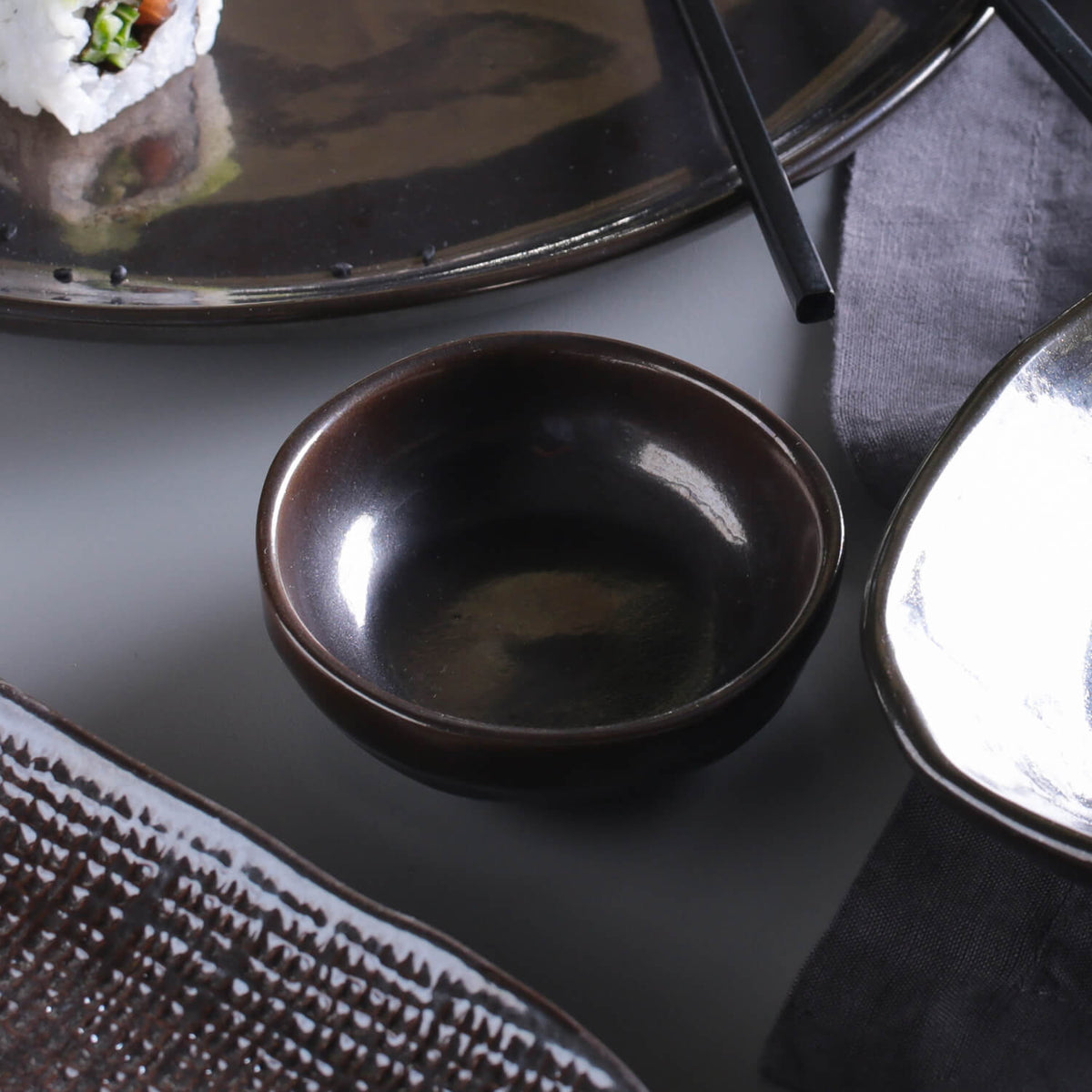 Dark ramekin on a gray surface near other dishes and table linens