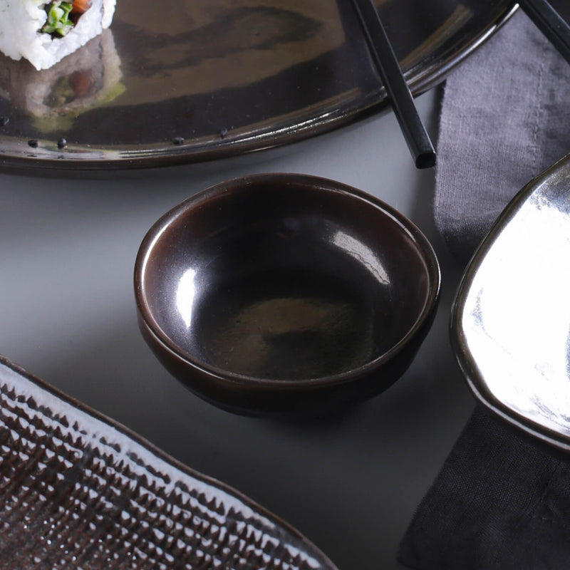 Dark ramekin on a gray surface near other dishes and table linens