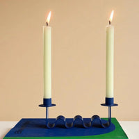 Blue candle holder with two lit candles on a beige background